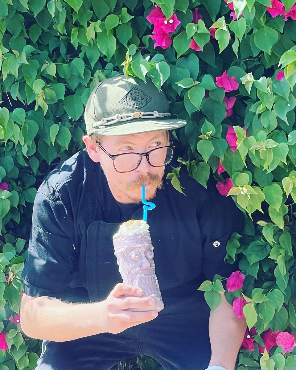 Golden Pineapple team member with a tiki cocktail in front of bougainvillea